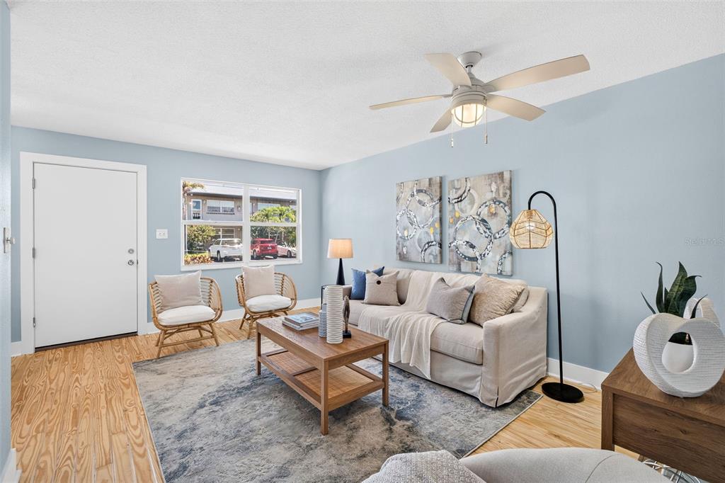 A living room features light blue walls, a ceiling fan, and a neutral sofa — 2 CAUSEWAY BOULEVARD UNIT 102, DUNEDIN, FL