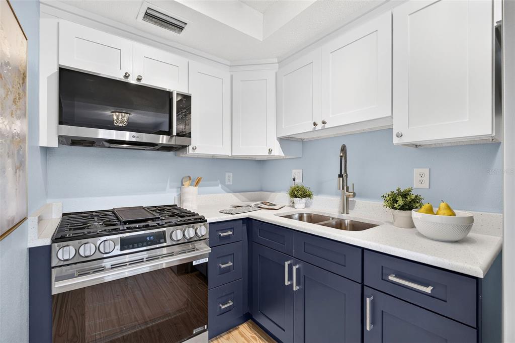 A kitchen features white upper cabinets, dark blue lower cabinets, a gas range, and countertops — 2 CAUSEWAY BOULEVARD UNIT 102, DUNEDIN, FL