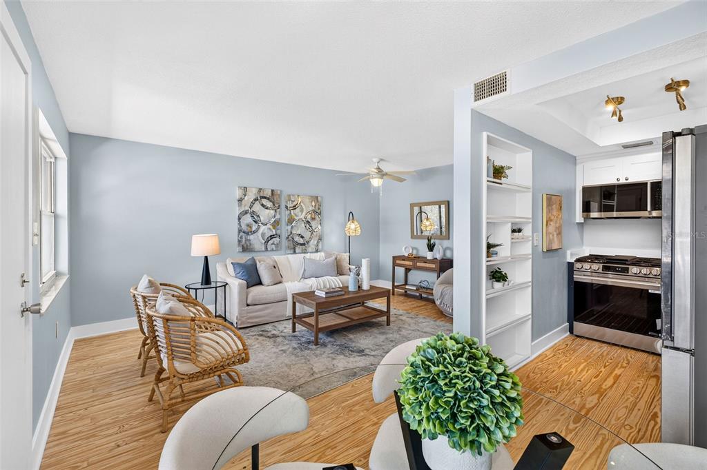 A living room with light blue walls, wood-look flooring, and an adjacent kitchen area — 2 CAUSEWAY BOULEVARD UNIT 102, DUNEDIN, FL