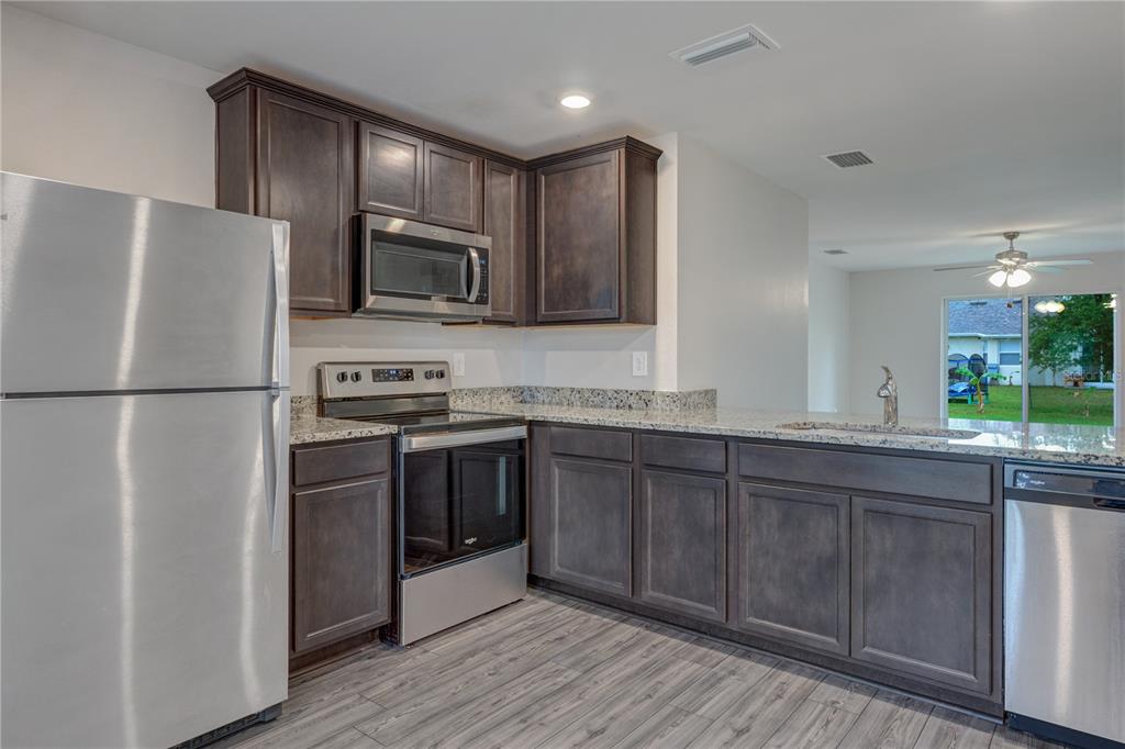 A kitchen features dark wood cabinets, stainless steel appliances, granite countertops, and wood-look flooring — 4127 SNOWDROP STREET, NORTH PORT, FL