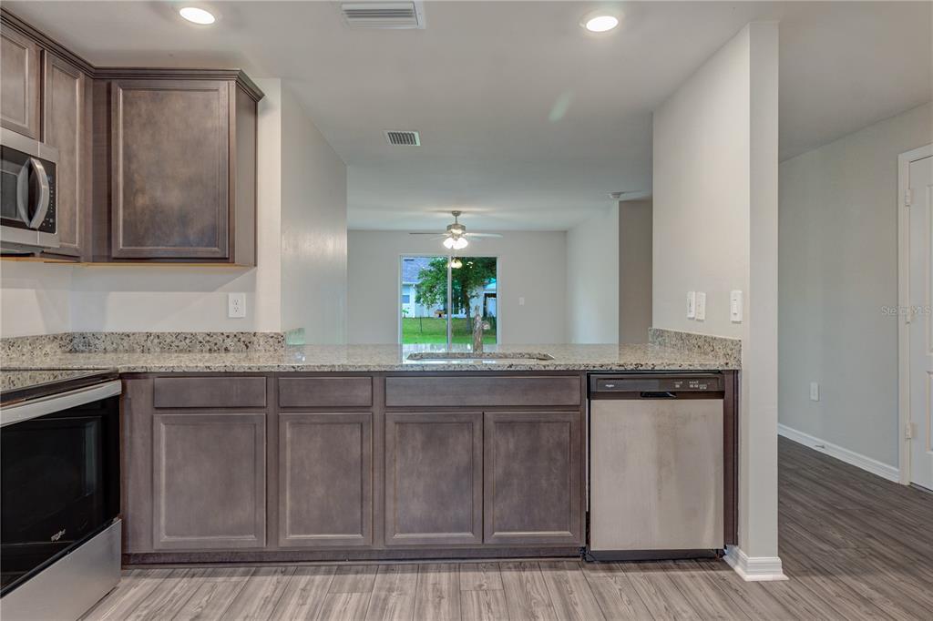 A kitchen features dark wood cabinets, granite countertops, stainless steel appliances, and wood-look flooring — 4127 SNOWDROP STREET, NORTH PORT, FL