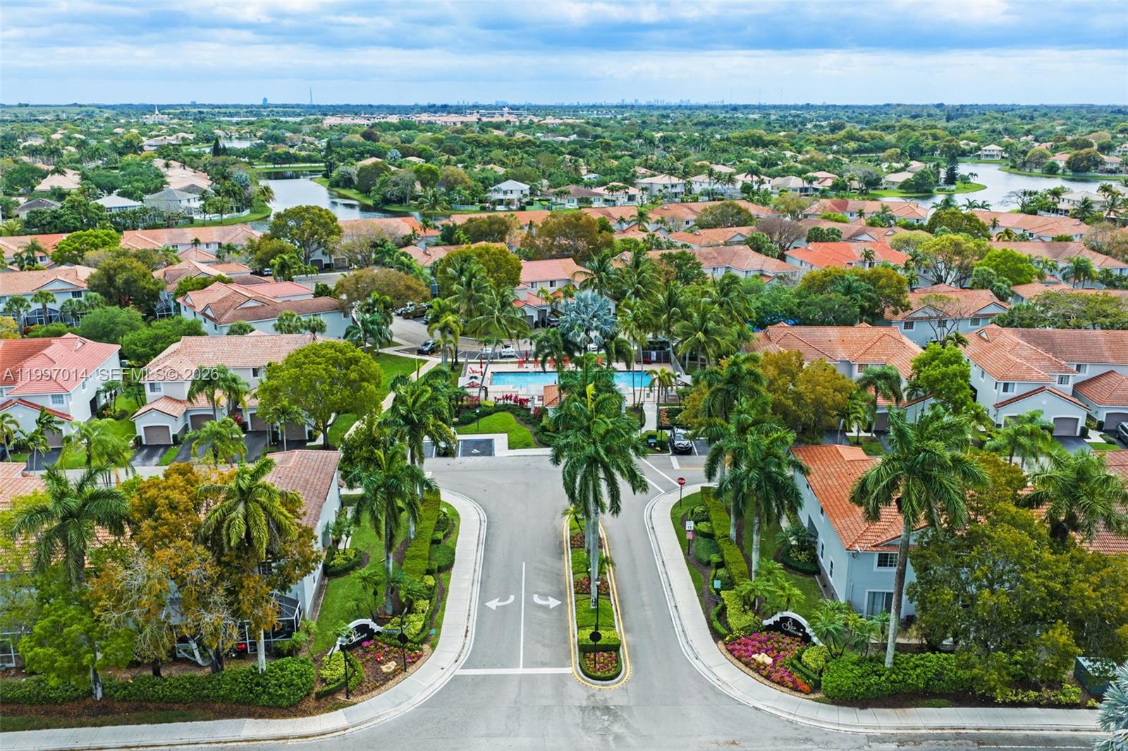 An aerial view shows a residential community entrance with palm trees, a swimming pool, and houses — 3676 San Simeon Cir, Weston FL 33331, WESTON, FL