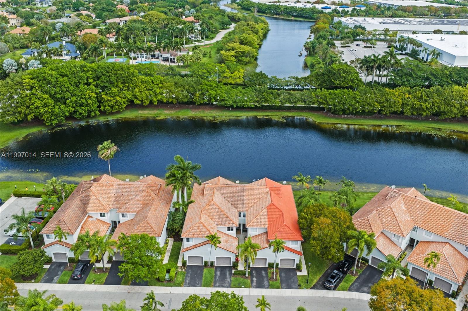 An aerial view shows three multi-story townhomes with orange tile roofs beside a lake — 3676 San Simeon Cir, Weston FL 33331, WESTON, FL