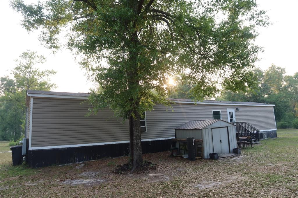 A tan mobile home with a metal storage shed sits beneath a large tree — 11533 E US 90, MADISON, FL
