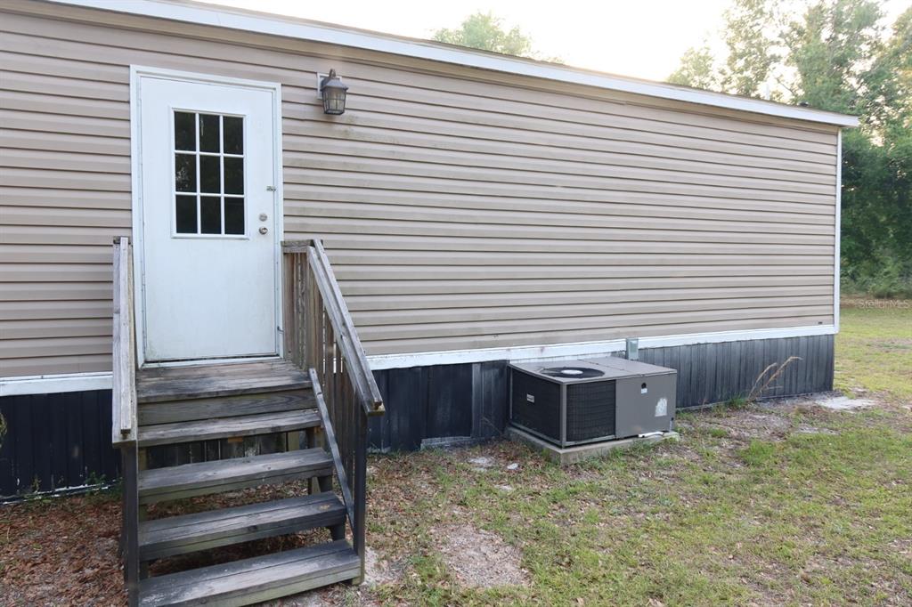 An exterior view of a mobile home with tan siding, a wooden staircase, and an AC unit — 11533 E US 90, MADISON, FL