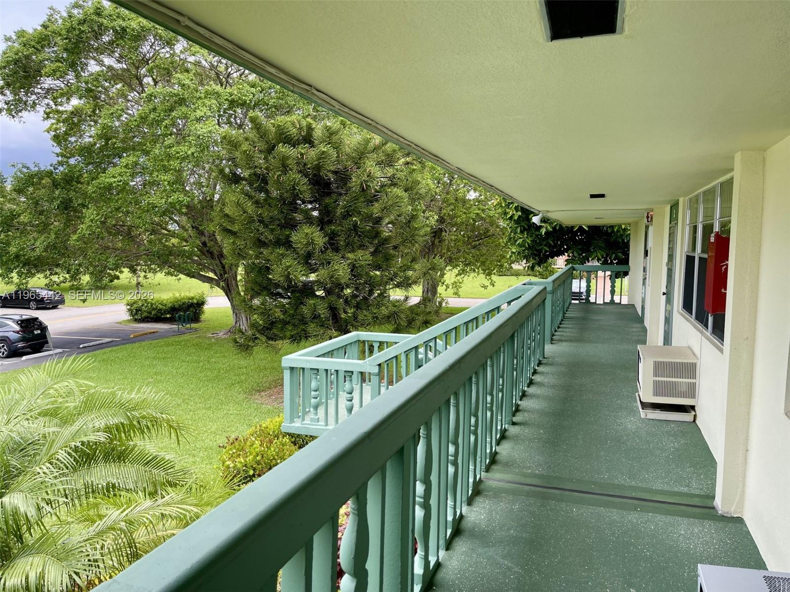 An outdoor balcony with a green railing overlooks a grassy area with trees and cars — 118 Upminster  E # 118, Deerfield Beach FL 33442, DEERFIELD BEACH, FL