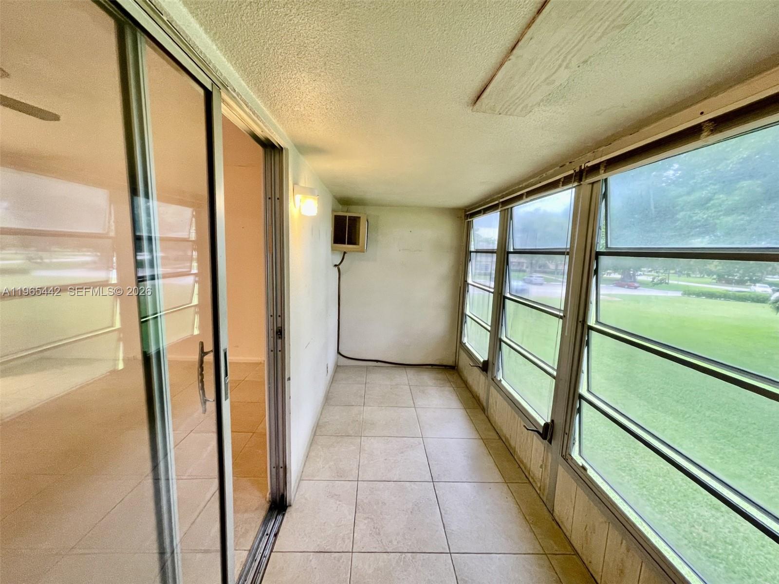 A sunroom with tile flooring, sliding glass doors, and large windows overlooking a grassy yard — 118 Upminster  E # 118, Deerfield Beach FL 33442, DEERFIELD BEACH, FL