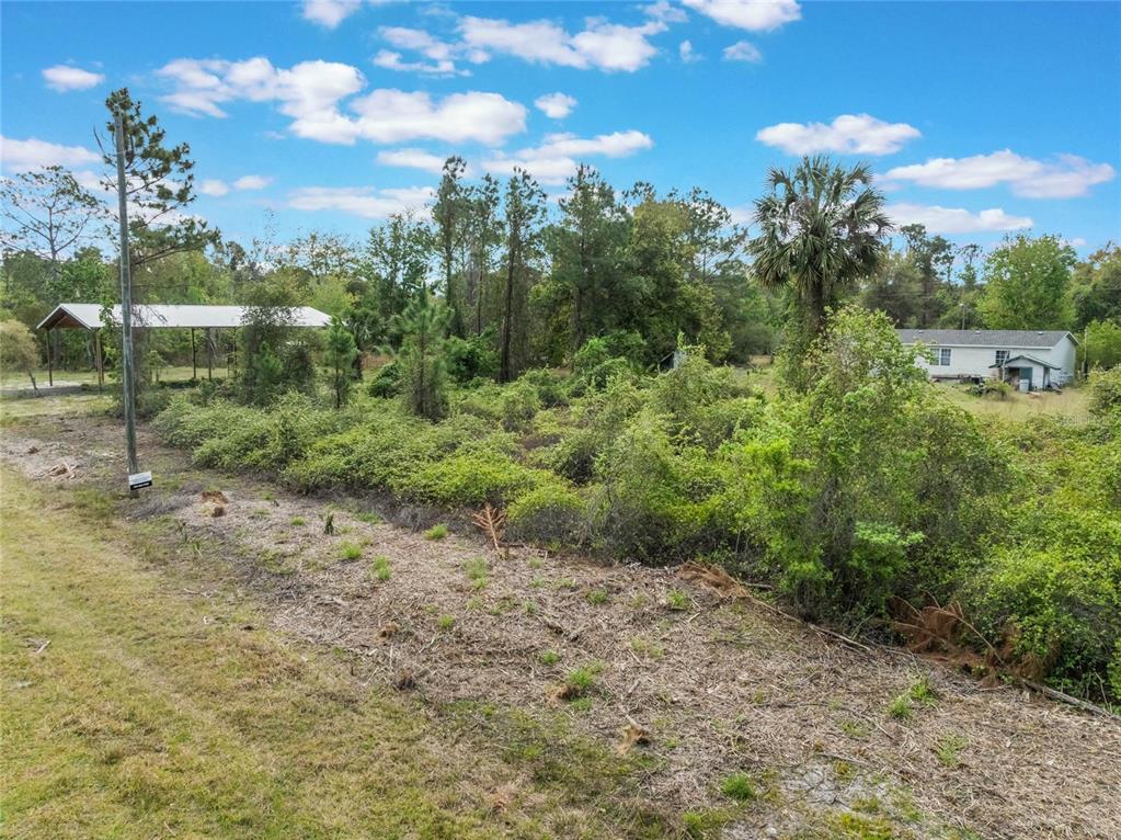 An overgrown, grassy lot features a metal carport and a small house in the background — 515 GARDENIA AVENUE, GEORGETOWN, FL
