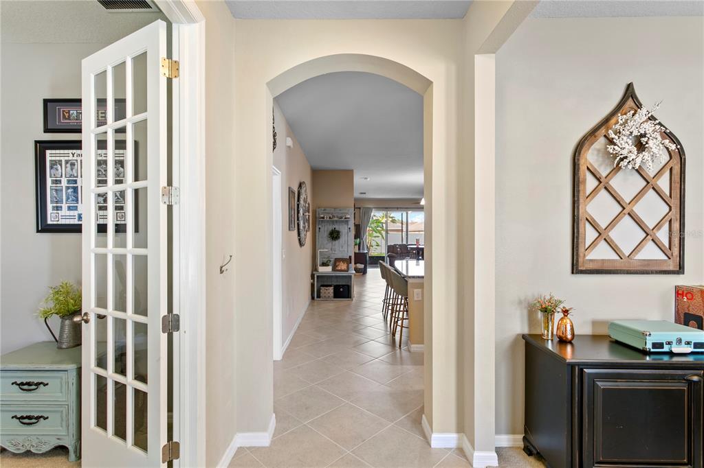 A hallway with tile flooring leads through an arched doorway toward an open-concept kitchen — 11412 LAKE LUCAYA DRIVE, RIVERVIEW, FL