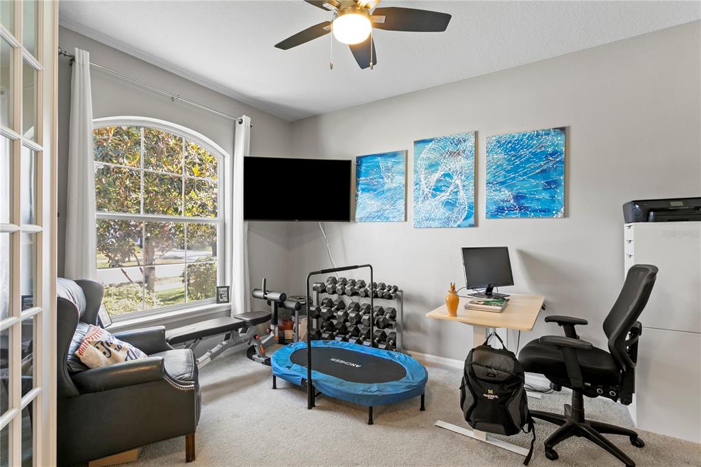 A home office features a desk, exercise equipment, a television, and a large arched window — 11412 LAKE LUCAYA DRIVE, RIVERVIEW, FL