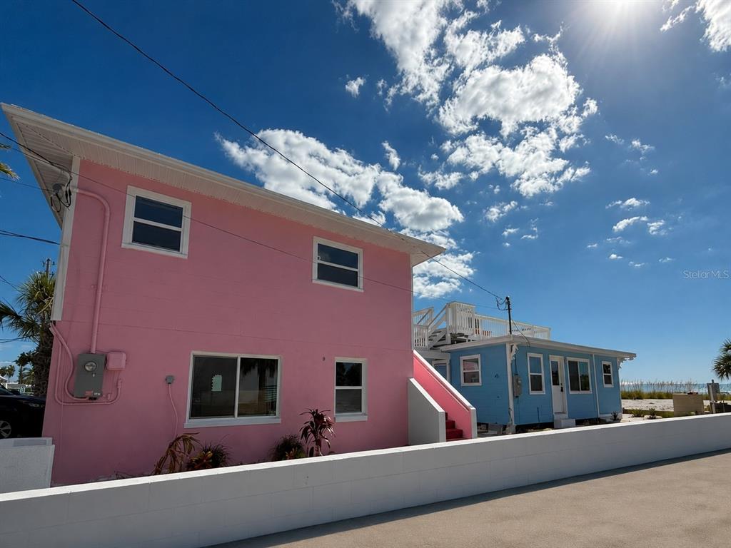 A pink two-story house stands next to a light blue house under a sunny sky — 12609 SUNSHINE LANE, TREASURE ISLAND, FL