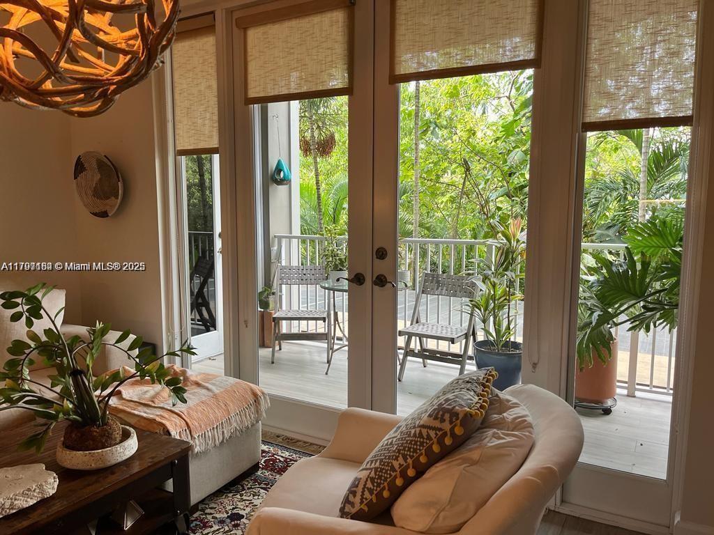 A living room features a beige armchair, a wooden coffee table, and glass doors opening onto a balcony — 3540 Main Hwy # 204, Miami FL 33133, MIAMI, FL