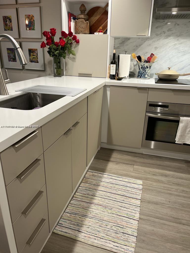 A modern kitchen features light-colored flat-panel cabinets, white countertops, stainless steel appliances, and wood-look flooring — 3540 Main Hwy # 204, Miami FL 33133, MIAMI, FL