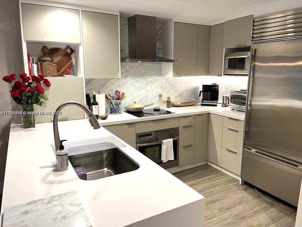 A modern kitchen features light gray cabinetry, white countertops, a stainless steel refrigerator, and marble backsplash — 3540 Main Hwy # 204, Miami FL 33133, MIAMI, FL