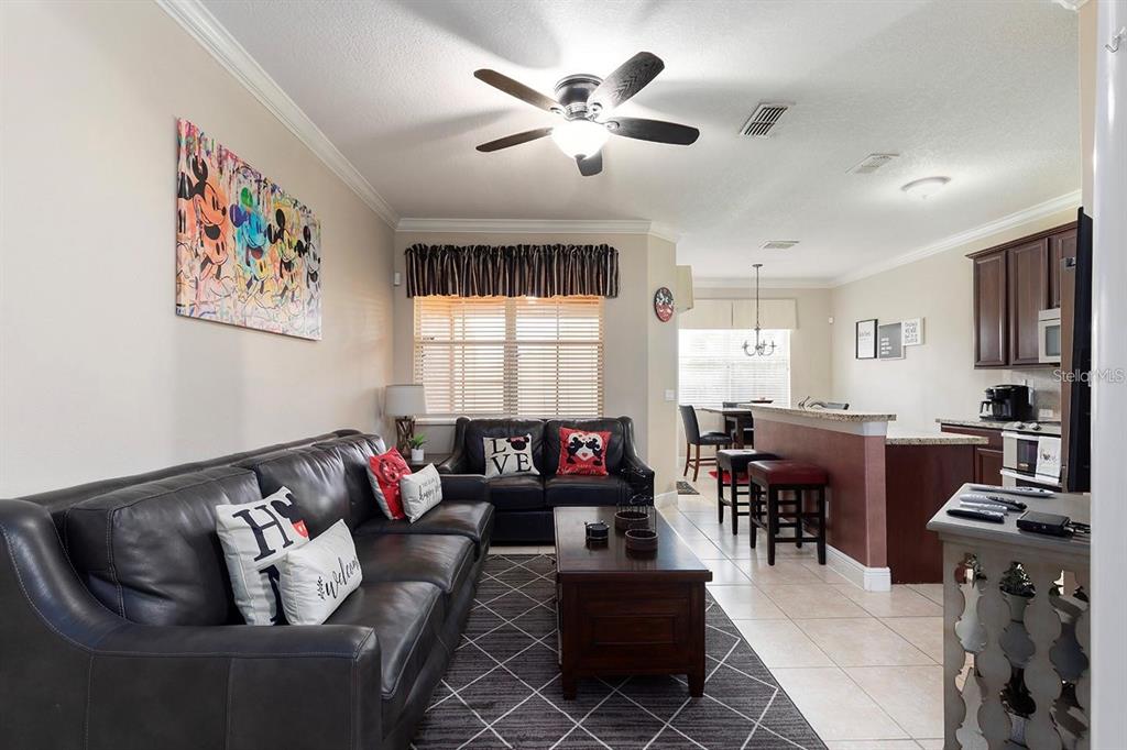 A living room with a black leather sofa, coffee table, and an open kitchen beyond — 7596 ASSEMBLY LANE, KISSIMMEE, FL