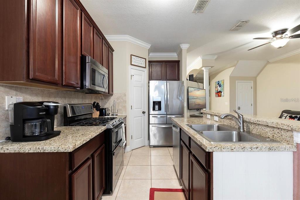 A kitchen features dark wood cabinets, granite countertops, stainless steel appliances, and tile flooring — 7596 ASSEMBLY LANE, KISSIMMEE, FL