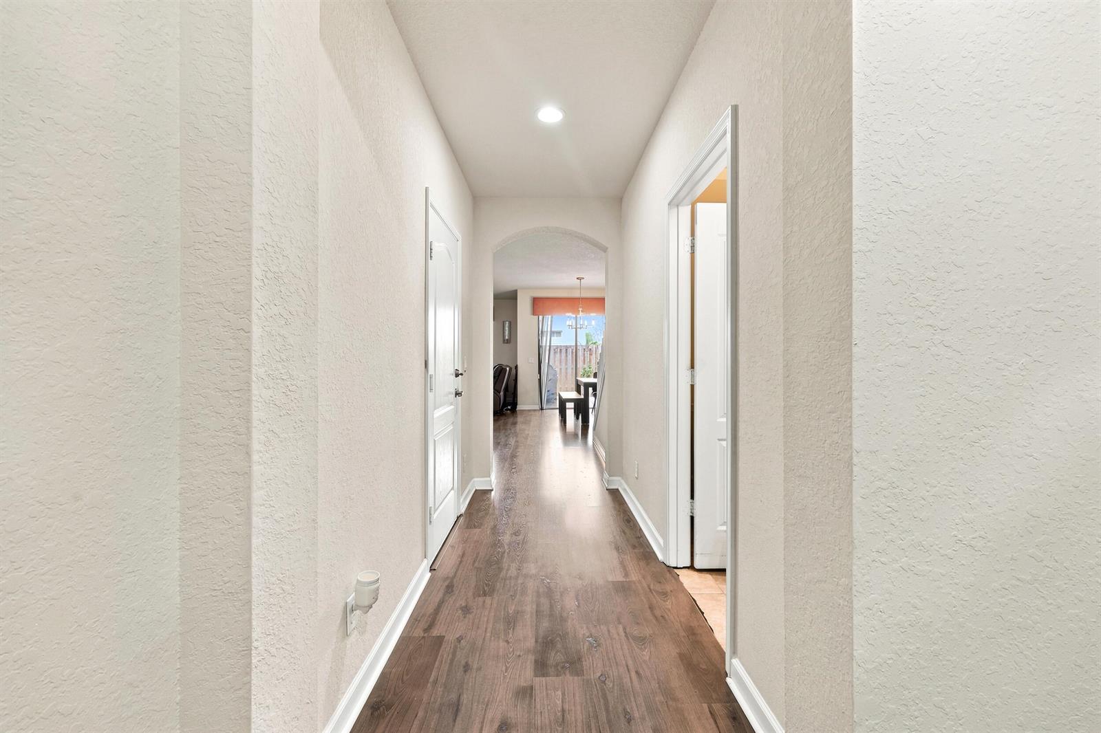 A hallway with wood-look flooring leads to an arched entryway opening into a dining area — 4310 Chalmers Lane, West Palm Beach FL 33417, WEST PALM BEACH, FL