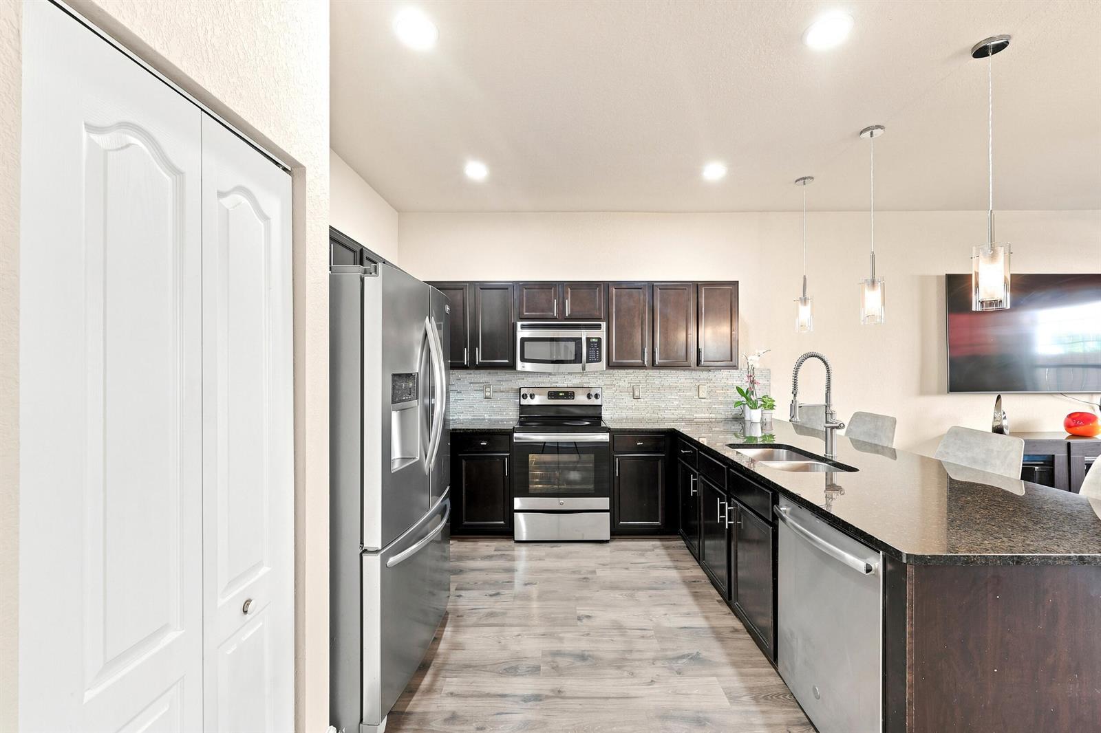A kitchen features dark wood cabinets, stainless steel appliances, granite countertops, and light wood flooring — 4310 Chalmers Lane, West Palm Beach FL 33417, WEST PALM BEACH, FL