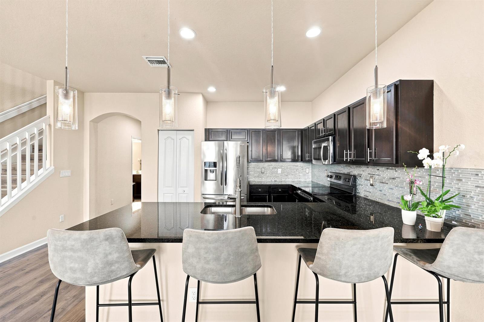 A kitchen features dark wood cabinets, black granite countertops, a center island, and bar seating — 4310 Chalmers Lane, West Palm Beach FL 33417, WEST PALM BEACH, FL