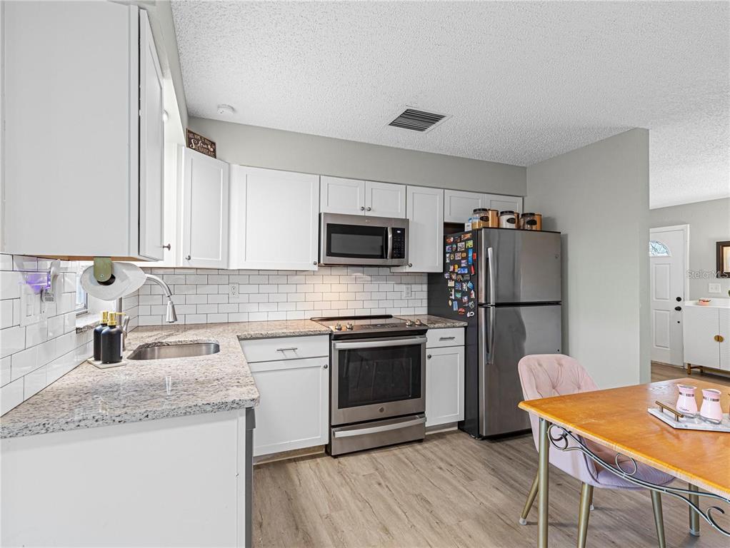 A kitchen features white cabinets, granite countertops, stainless steel appliances, and light wood-look flooring — 3124 LECANTO STREET, HOLIDAY, FL
