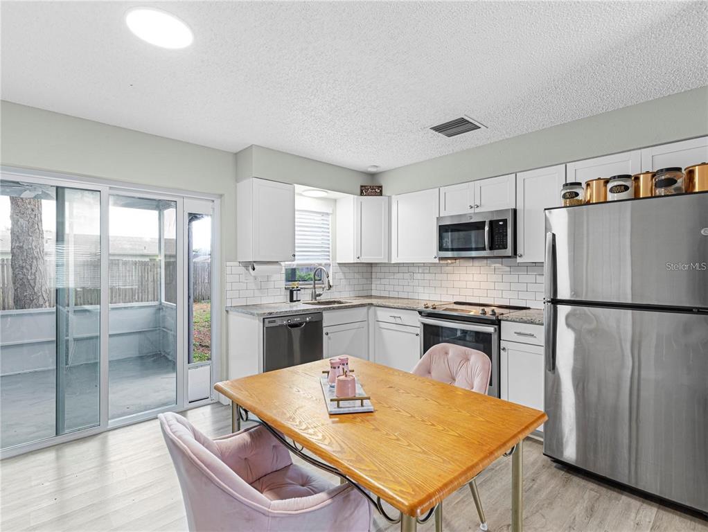 A kitchen with white cabinets, stainless steel appliances, and a wooden dining table with chairs — 3124 LECANTO STREET, HOLIDAY, FL