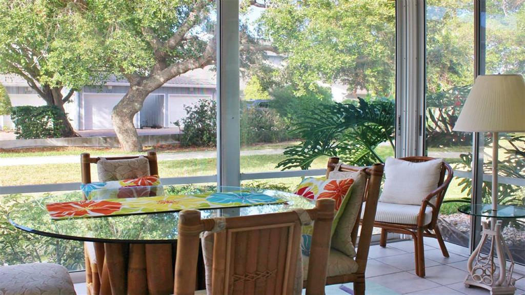 A sunroom features a glass-topped dining table, rattan chairs, and large windows overlooking a yard — 1241 SIESTA BAYSIDE DRIVE UNIT 1241-A, SARASOTA, FL