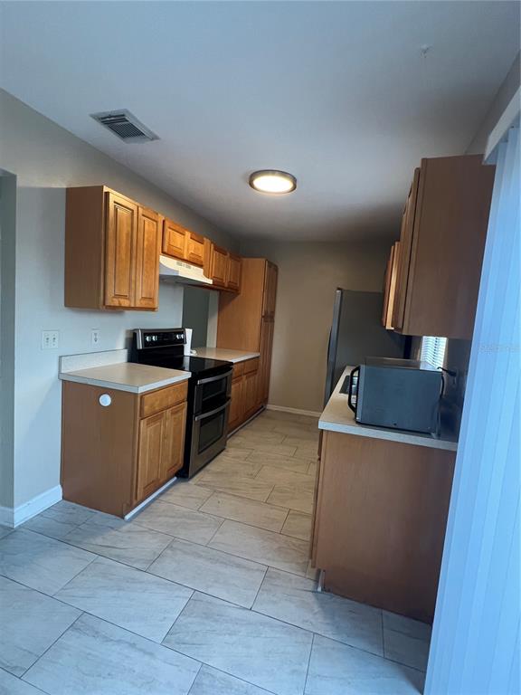 A kitchen features wood cabinets, stainless steel appliances, and light-colored tile flooring — 6231 YORKTOWN DRIVE UNIT 140, ORLANDO, FL