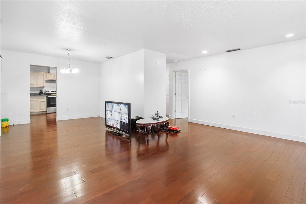 A living room with hardwood floors, white walls, and a television on a small table — 1700 NEEDLEWOOD LANE, ORLANDO, FL