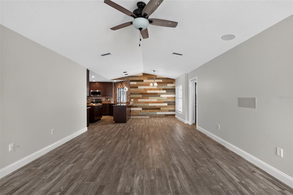 A living area with wood-look flooring, a vaulted ceiling, and a wood-plank accent wall — 12421 WINDSWEPT AVENUE, RIVERVIEW, FL
