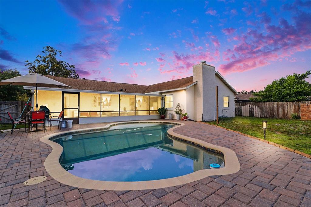A backyard features a swimming pool, a brick patio, and a screened-in porch at sunset — 3641 HAWTHORNE LANE, WINTER PARK, FL