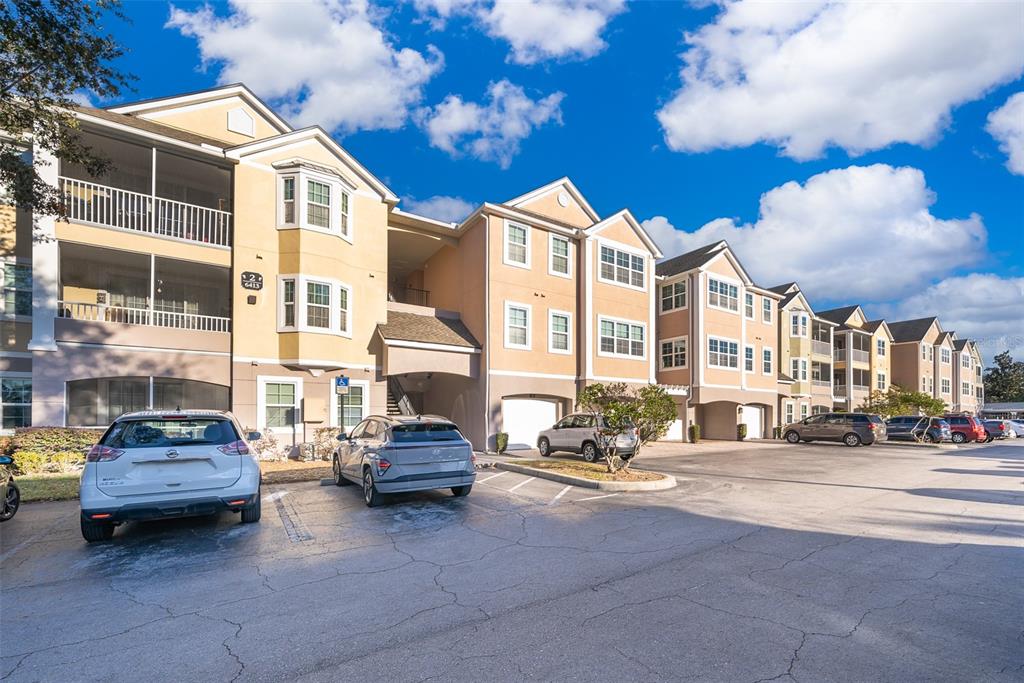 Exterior view of a multi-story apartment complex with a parking lot in the foreground — 6413 ASTOR VILLAGE AVENUE UNIT 305, ORLANDO, FL