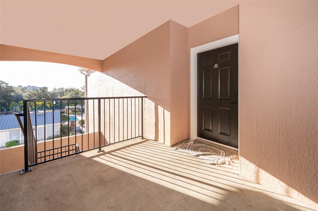 A covered outdoor balcony features a black front door, a metal railing, and concrete flooring — 6413 ASTOR VILLAGE AVENUE UNIT 305, ORLANDO, FL