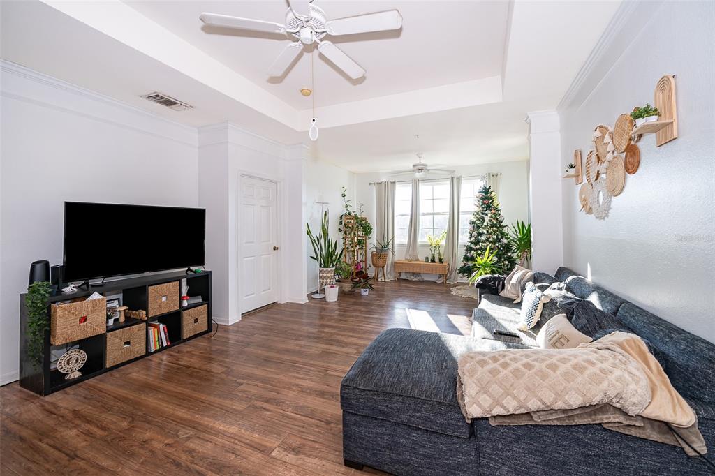 A living room features a dark sectional sofa, a television on a storage unit, and plants — 6413 ASTOR VILLAGE AVENUE UNIT 305, ORLANDO, FL