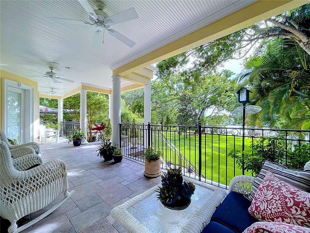 A covered patio features white wicker furniture, stone flooring, and a view of the lawn — 3312 N PERRY AVENUE, TAMPA, FL