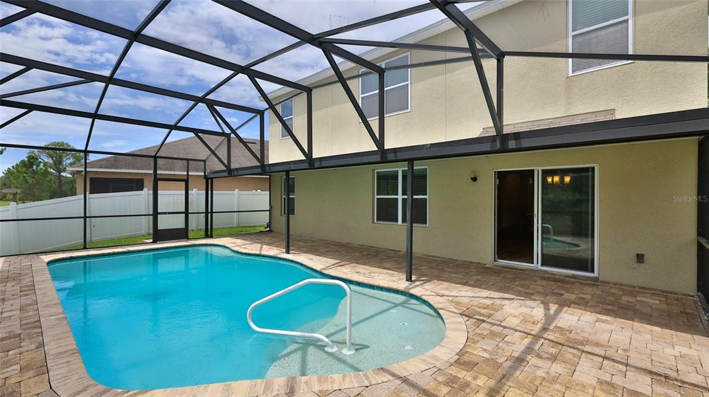 A backyard features a swimming pool with a white handrail inside a screened-in patio enclosure — 441 WHITE CORAL DRIVE, NEW SMYRNA BEACH, FL