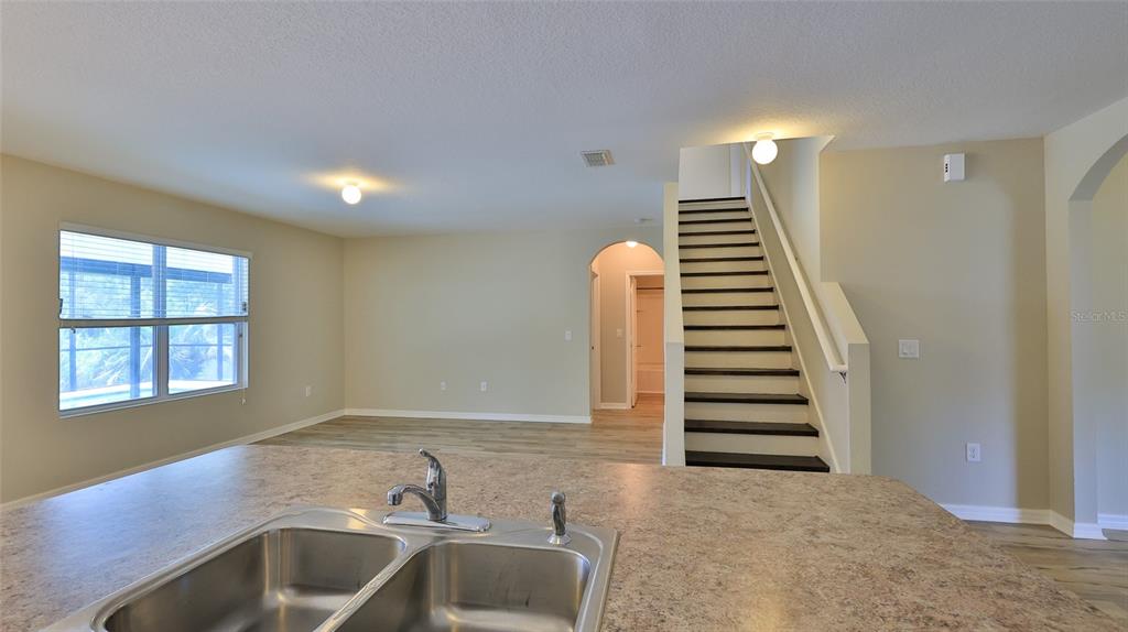 A kitchen island with a double sink overlooks a living area with stairs and flooring — 441 WHITE CORAL DRIVE, NEW SMYRNA BEACH, FL