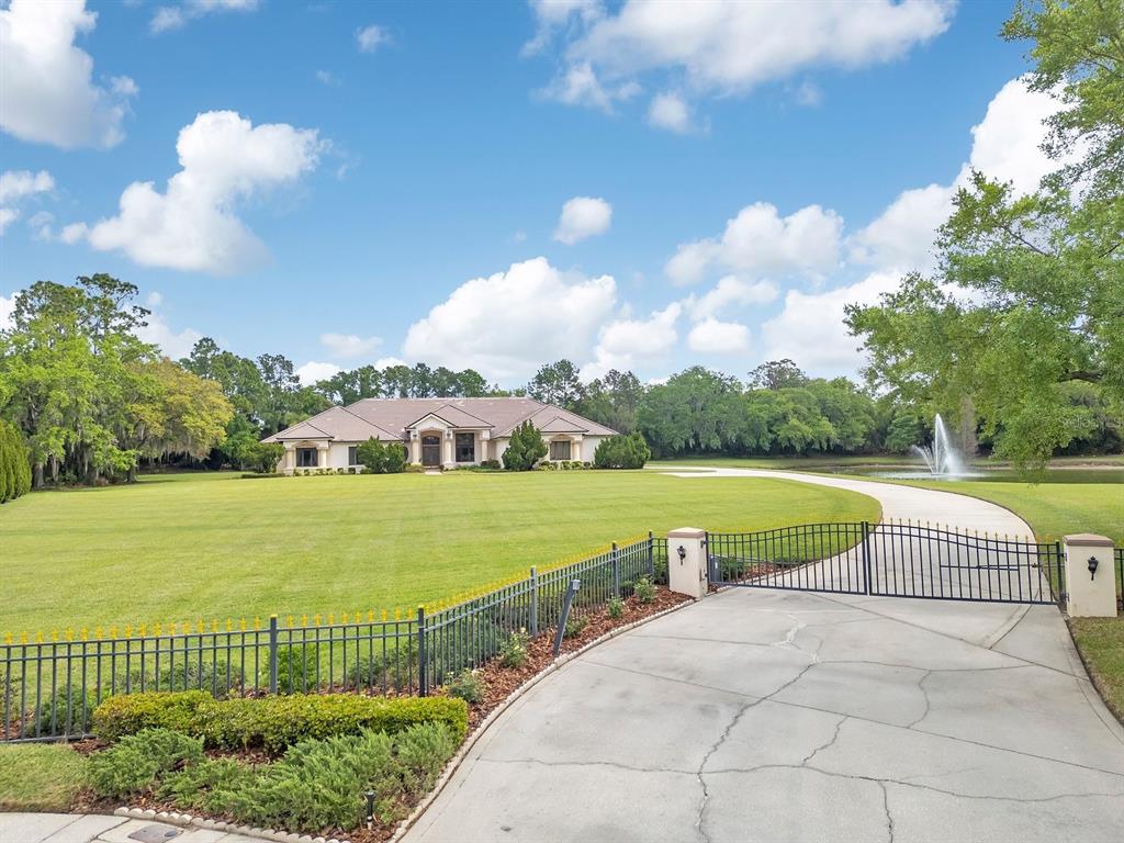 A gated concrete driveway leads to a single-story house with a large lawn and fountain — 3300 BRIDGEFIELD DRIVE, LAKELAND, FL