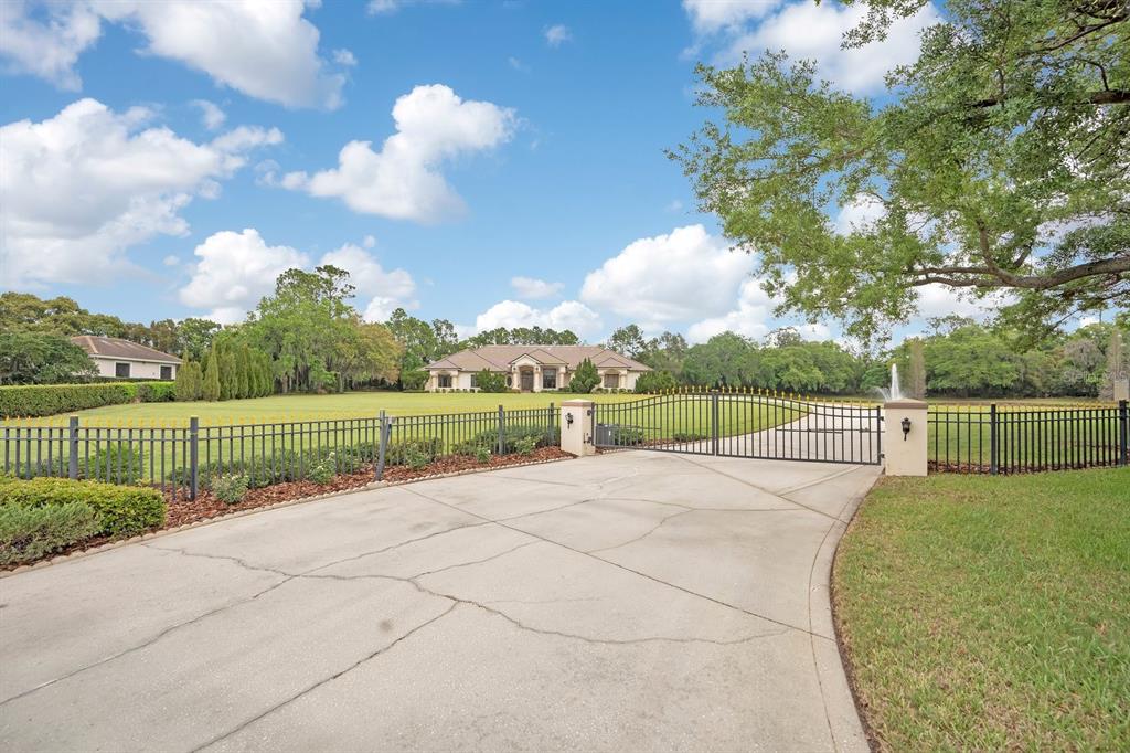 A gated concrete driveway leads to a large house set back on a grassy lawn — 3300 BRIDGEFIELD DRIVE, LAKELAND, FL