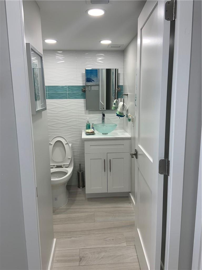 A small bathroom features a white vanity, a glass vessel sink, and textured wall tiles — 133 N Pompano Beach Boulevard # 507, Pompano Beach FL 33062, POMPANO BEACH, FL