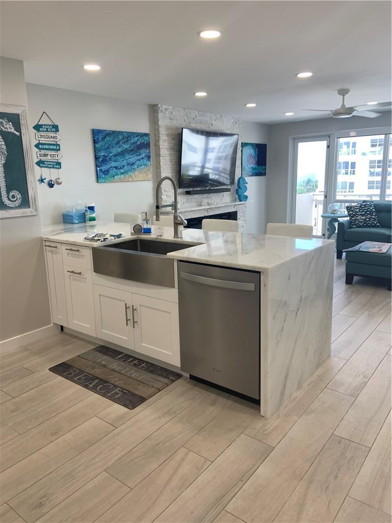 A kitchen island with a farmhouse sink and dishwasher faces a living area with fireplace — 133 N Pompano Beach Boulevard # 507, Pompano Beach FL 33062, POMPANO BEACH, FL