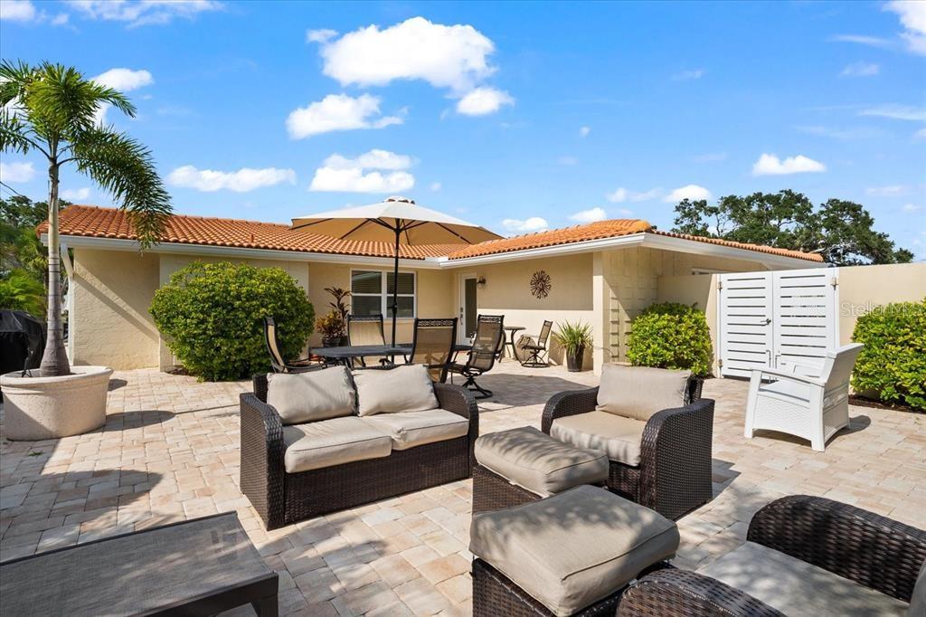 A paved patio features outdoor wicker furniture, a dining set with an umbrella, and landscaping — 327 AVENIDA MILANO, SARASOTA, FL