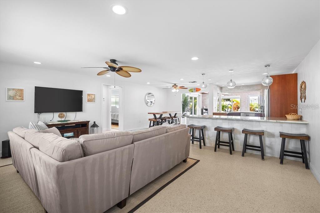 A living room with a sectional sofa and television opens to a kitchen with bar seating — 327 AVENIDA MILANO, SARASOTA, FL