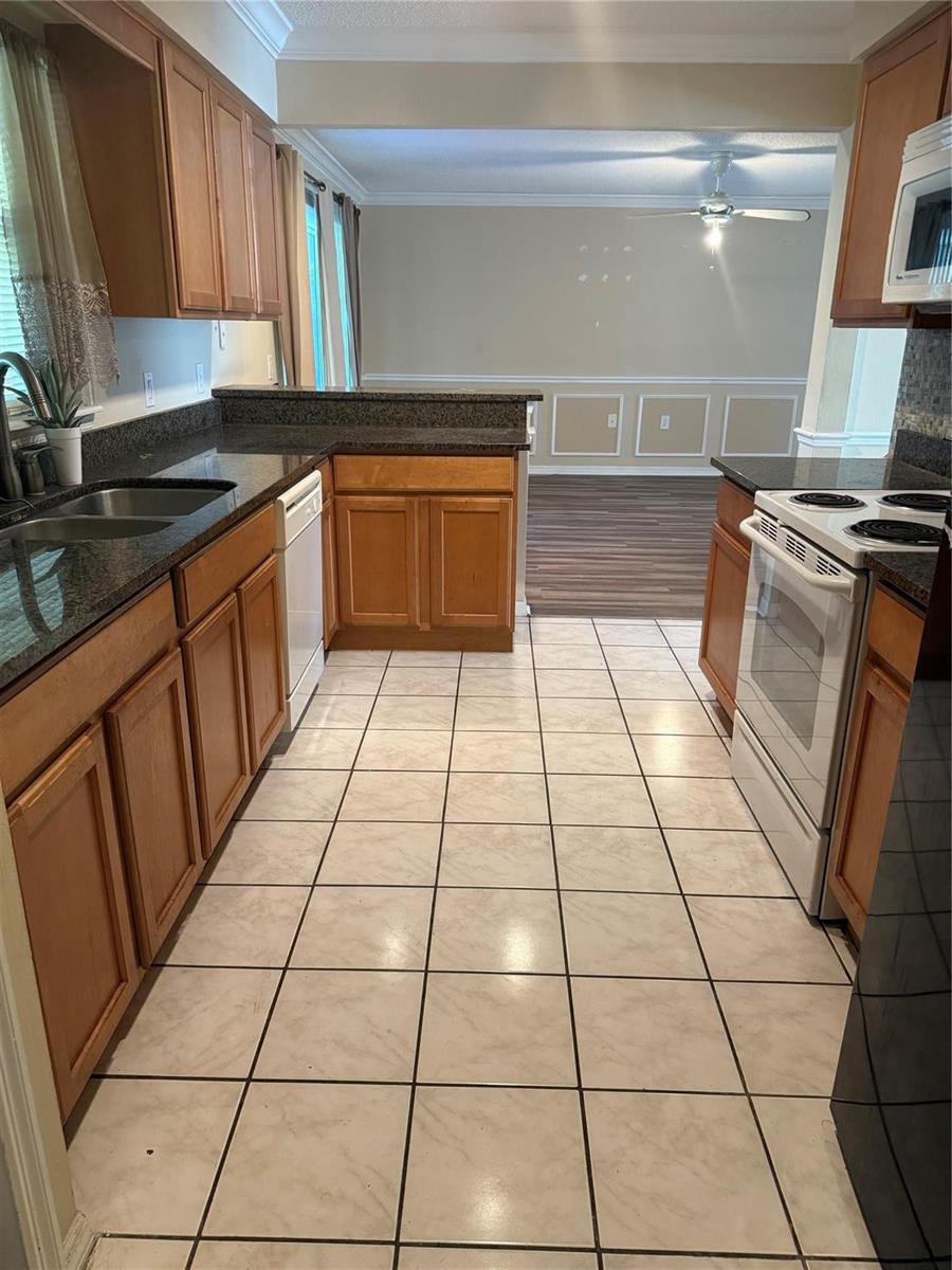 A kitchen with wood cabinets, dark granite countertops, white appliances, and light-colored tile flooring — 7821 Shellbark Drive, Orlando FL 32818, ORLANDO, FL
