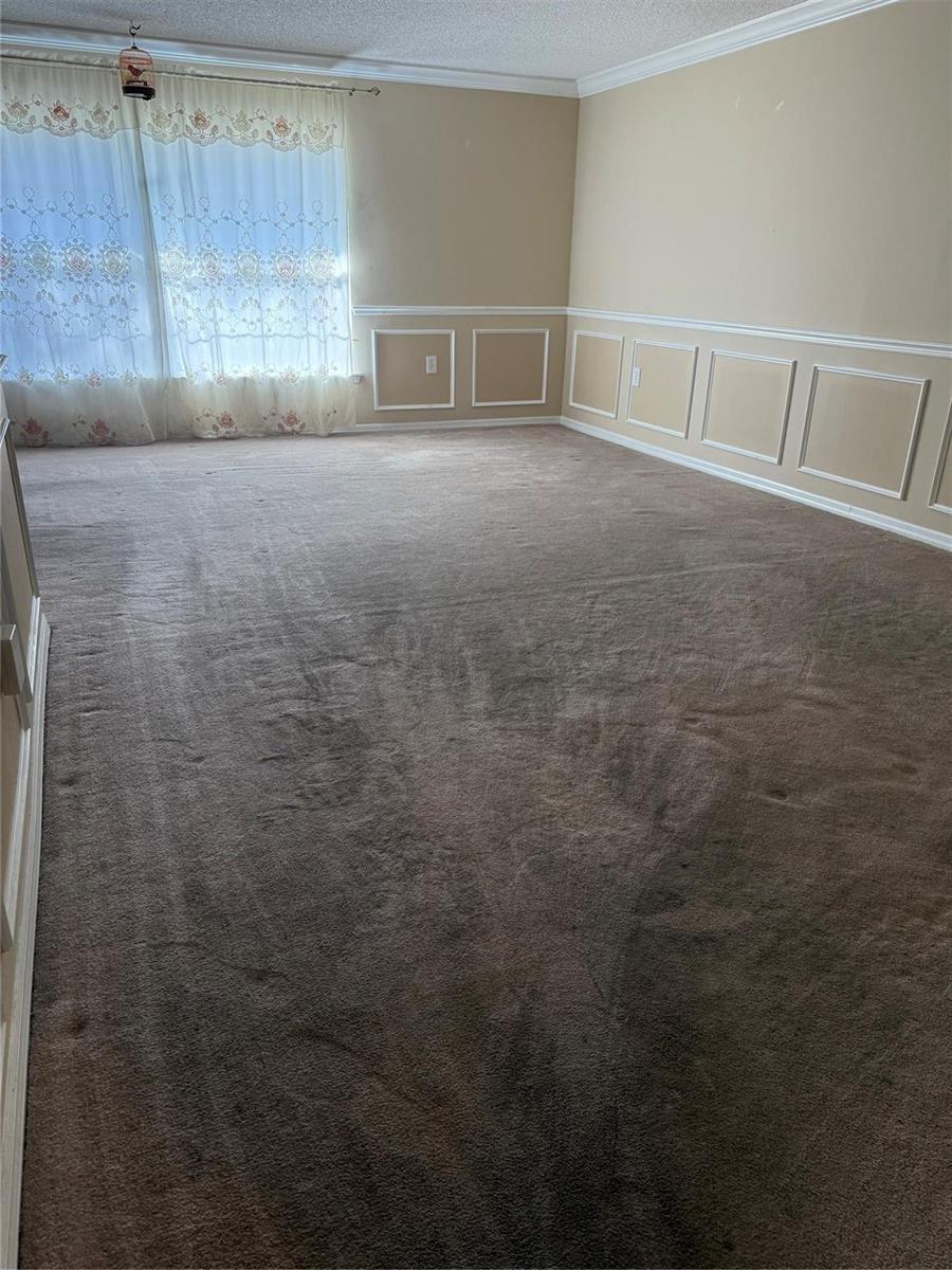 An empty room features brown carpeting, beige walls with wainscoting, and sheer floral curtains — 7821 Shellbark Drive, Orlando FL 32818, ORLANDO, FL