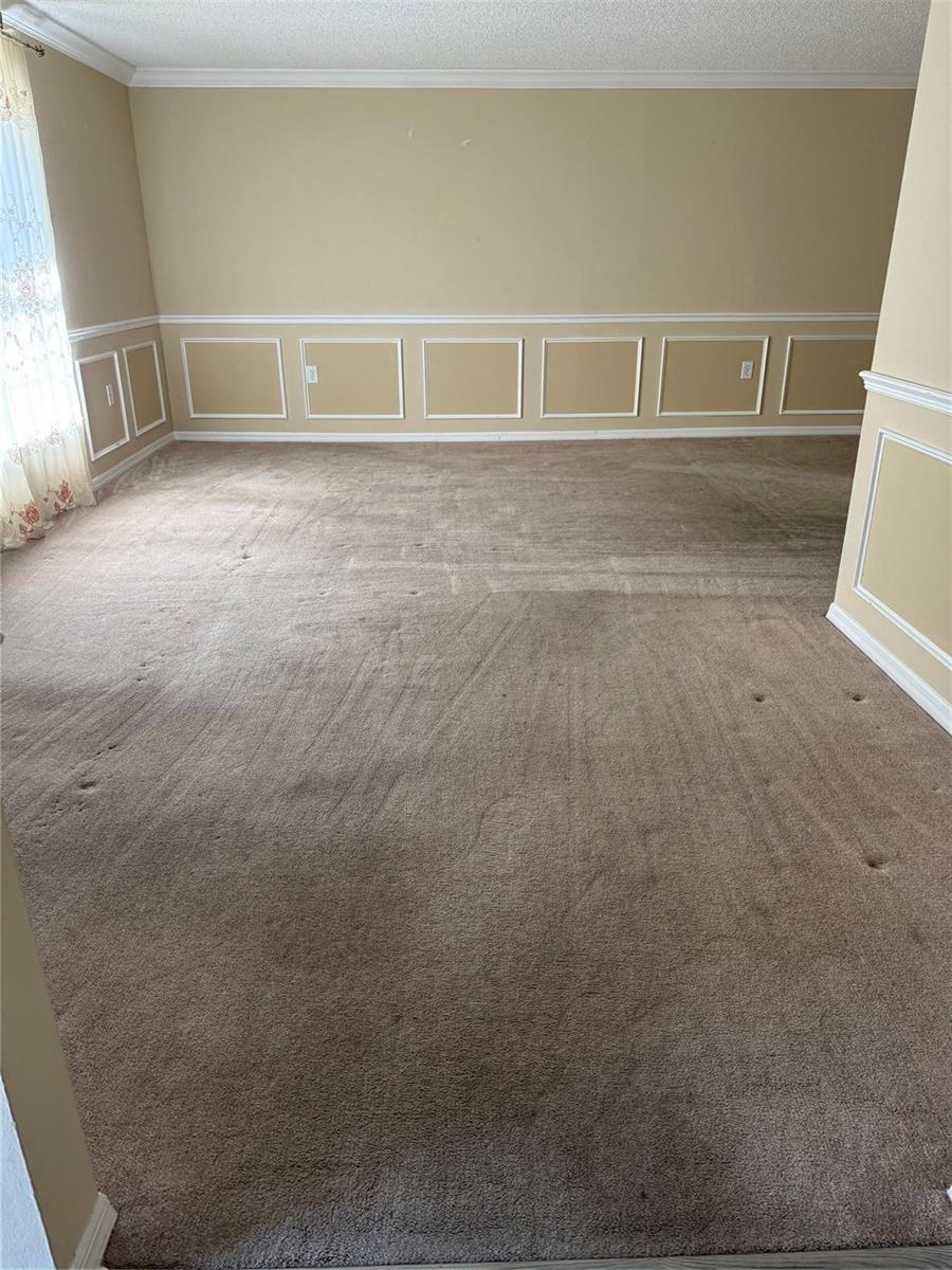 An empty room features beige carpet, tan walls, and white wainscoting trim — 7821 Shellbark Drive, Orlando FL 32818, ORLANDO, FL