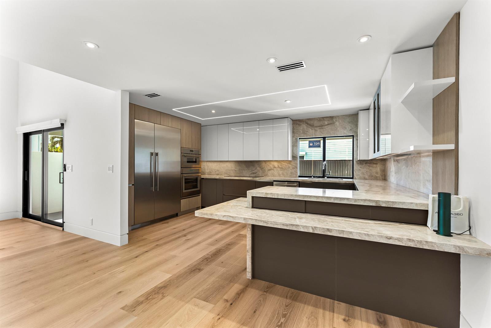A modern kitchen features two-tone cabinetry, stone countertops, stainless steel appliances, and light wood flooring — 1692 S Ocean Boulevard, Delray Beach FL 33483, DELRAY BEACH, FL