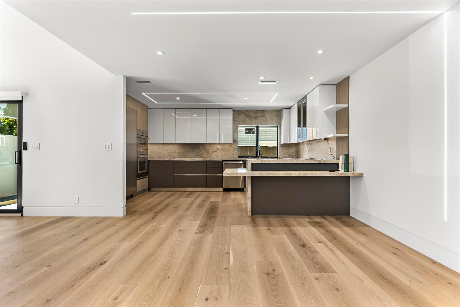 A modern kitchen features white and dark cabinetry, stone countertops, and light wood flooring — 1692 S Ocean Boulevard, Delray Beach FL 33483, DELRAY BEACH, FL