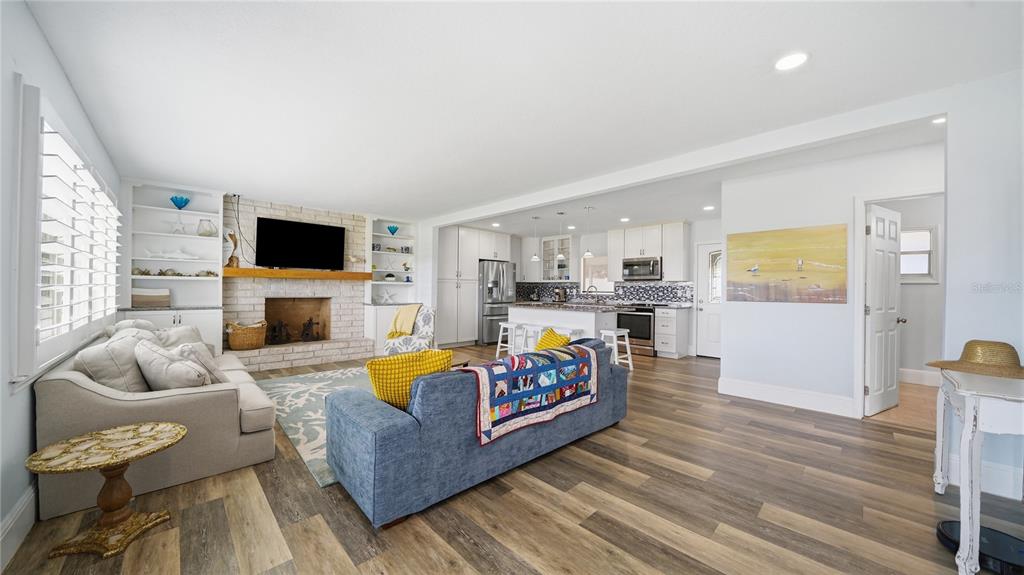 An open-concept living room and kitchen feature wood-look flooring, a brick fireplace, and white cabinetry — 26 OCEAN VISTA LANE, PALM COAST, FL