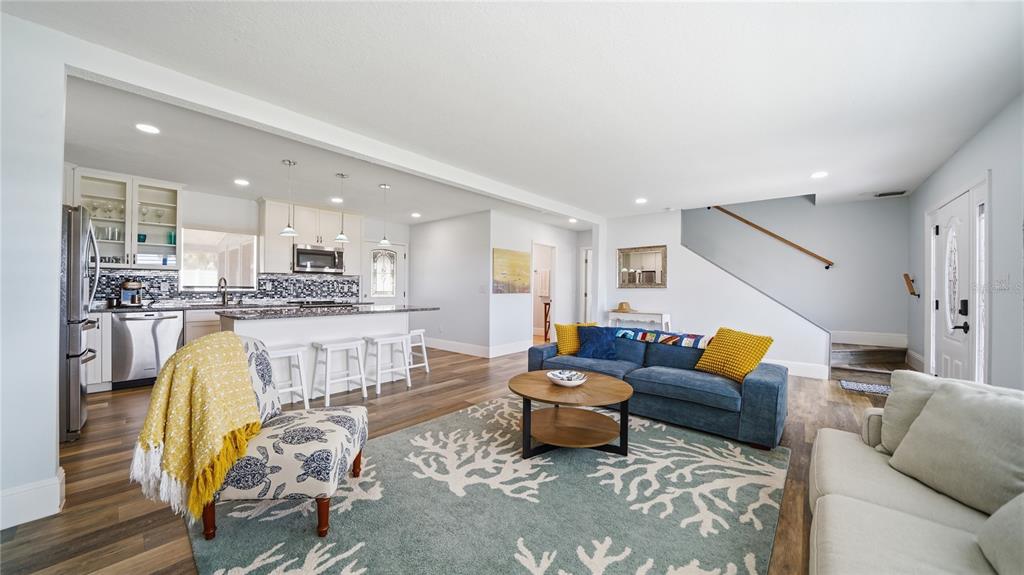 An open-concept living room and kitchen featuring hardwood floors, a blue sofa, and white cabinetry — 26 OCEAN VISTA LANE, PALM COAST, FL
