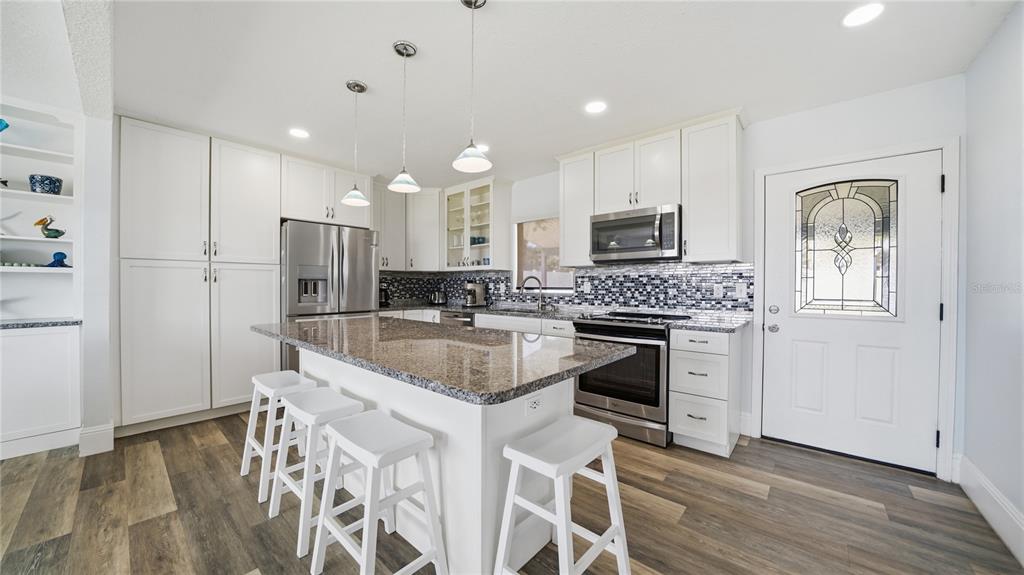 A modern kitchen features white cabinetry, a granite-topped island with stools, and stainless steel appliances — 26 OCEAN VISTA LANE, PALM COAST, FL